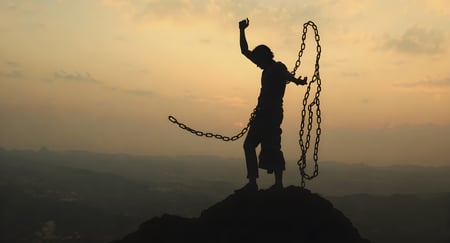 A graphic of an individual casting off chains, standing atop a mountain before a wide landscape.